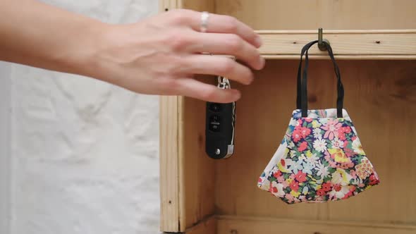 Female hand picking up floral face mask and car keys, going out and leaving house in new normal conc alt