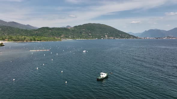 Low aerial orbit of a boat anchored on a giant mountain lake with buoys tree covered hills, distant alt