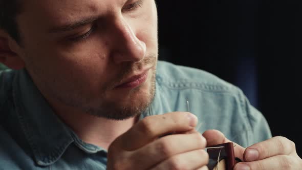 Young Man Tailor Sewing Two Pieces of Leather on Stand Closeup Using Professional Sharp Needle and alt