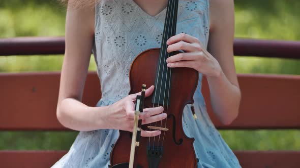 A Young Girl Holds a Violin in Her Hand and Touches the Strings alt
