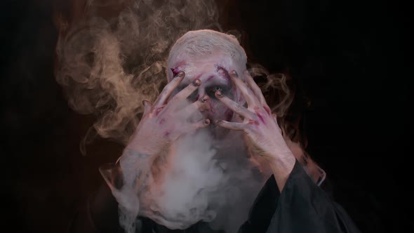 Sinister Man with Horrible Scary Halloween Zombie Makeup in Costume Blows Smoke From Nose and Mouth alt