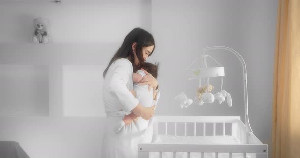 Mother Holds a Newborn Baby in Her Arms Kisses Him and Puts Him in a Crib