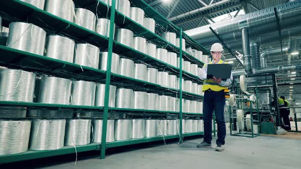 Factory Worker with a Laptop Next to the Shelves with Fiberglass alt