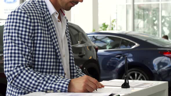The Serious Buyer Signs the Documents on the Purchase of the Car