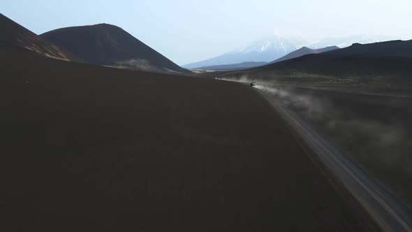 cars drive on black earth overlooking volcanoes