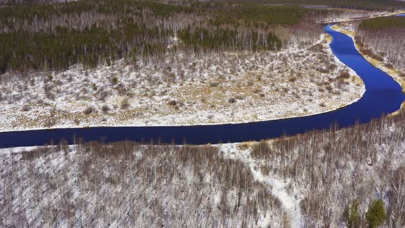 Aerial footage the river flows in the forest among the snowy shores in Sunny weather. alt