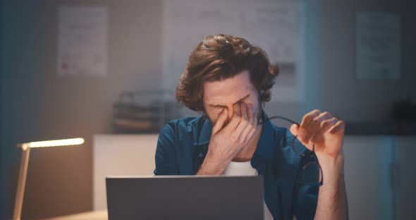 Young Businessman Having Headache Working Overtime with Laptop at Office Late Night alt