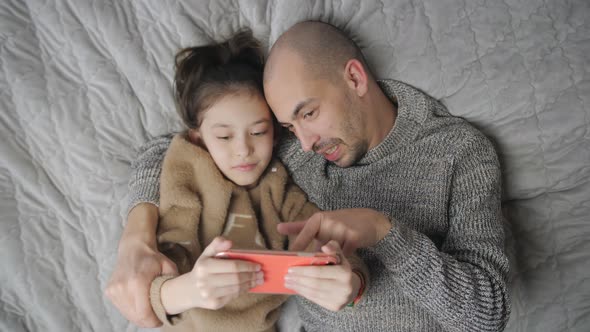 Top View of Joyful Dad with Little Daughter Lying Down Together on Bed Bedding Smiling Looking on