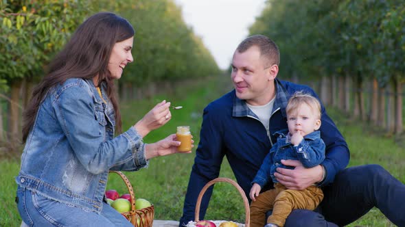Children Food Mother Feeds Little Son with Spoon with Fruit Puree in a Jar While Sitting in His alt