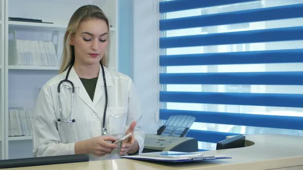 Pretty Nurse Using Tablet and Phone at Hospital Reception Desk alt