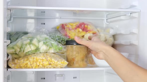 Female Hands take out containers with frozen soup in the fridge.