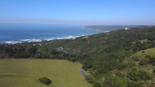 Drone shot of Wilderness hills in South Africa - drone is flying over some farms towards the beach a alt