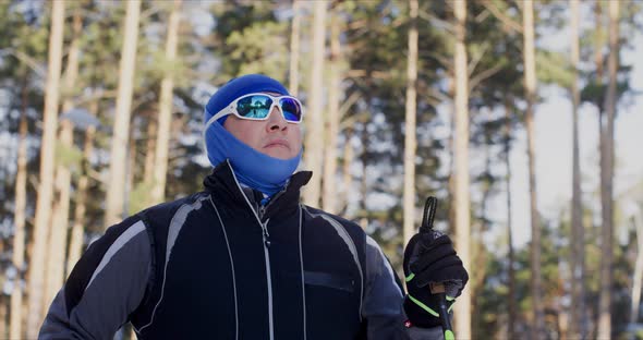 Man Skier in Winter Outfit is Standing and Looking Forward on Forest Background