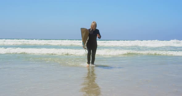 Front view of active senior Caucasian female surfer running on sea in the sunshine 4k alt