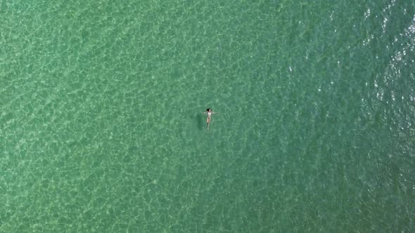 A young woman in a bikini swims on her back in the green waters of the Aegean Sea; Paros island, Gre alt