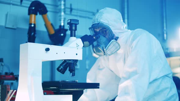 Male Specialist in a Hazmat Suit is Operating a Microscope alt