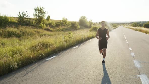 Young Sportsman Jogging and Looking Asides on a Race Out of City During Sunset alt