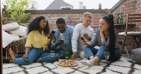 Friends which Sitting on the Carpet in the Balcony and Using thier Smartphones During Summer Party alt
