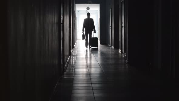 Silhouette of Businessman Walking with Luggage along Hotel