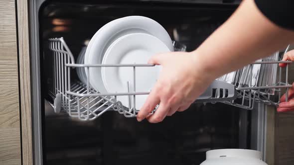 Female Hands Extract Basket of Dishwasher Takes Washed Plate From Open Machine alt