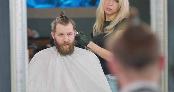 Rreflection in the Mirror of a Young Bearded Man Who is Sitting on the Barber's Chair Facing the alt