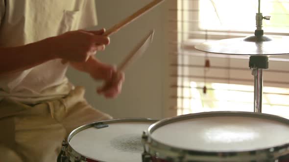Drummer practicing ghost note rudiments with natural light coming through the window. alt