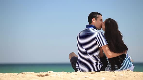 Young couple sits on sand on the beach in summer day.