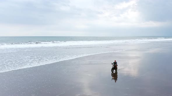 Man in Riding Motorcycle on Beach. Vintage Motorbike on Beach Sunset on Bali. Young Hipster Mal alt