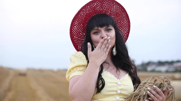 A Beautiful Sweet Brunette Woman in a Field with Hay on a Haystack in a Yellow Stylish Dress