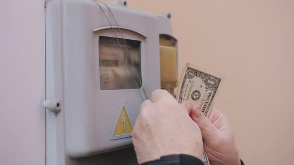A Man Counts Small Bills Against the Background of an Electricity Meter