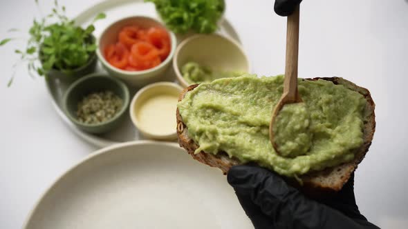 Cook Spreads Guacamole on Toast with Wooden Tablespoon alt