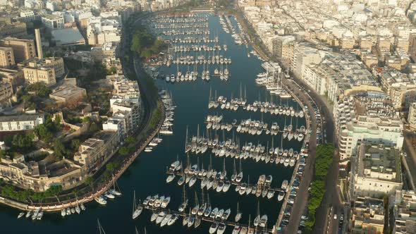 Sailboats and Regular Boats Sitting in Marina Port on Malta Island, Aerial Tilt Down View alt