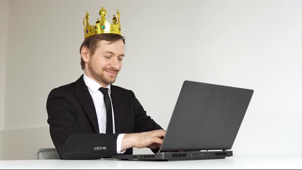 Self-confident arrogant businessman with golden crown on head using laptop.