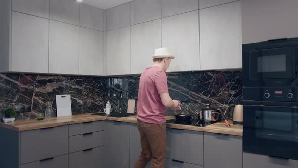 Young Man in a Hat Dancing and Singing in the Kitchen While Cooking alt