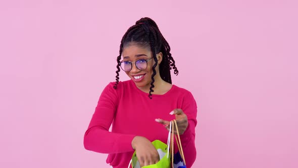 AfricanAmerican Girl in Pink Clothes Looks in Paper Laminated Bags with Handles and Shows the alt