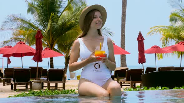 Young Attractive Woman in Straw Hat Drink Orange Cocktail in Outdoor Swimming Pool in Hotel alt