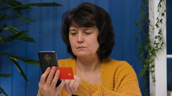 Middle Aged Woman Uses Mobile Phone for Online Shopping and Holding Credit Card at Home alt