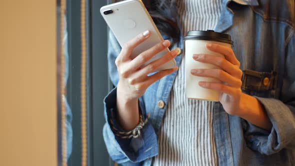 Businesswoman using smartphone beside a window at the office.