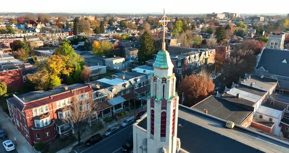 Aerial orbit of Christian church with steeple and cross, crucifix. Fall foliage during golden hour. alt