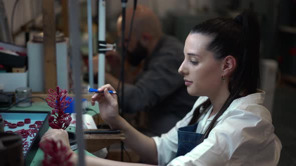 Side View Tired Young Woman Rubbing Forehead Working in Jewellery Workshop with Blurred Man at alt