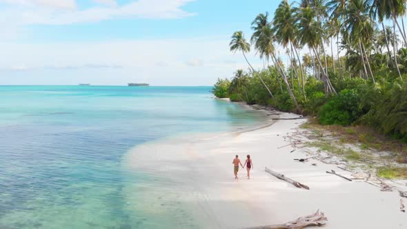 Aerial slow motion: couple walking on tropical beach at sunset, away from it all alt