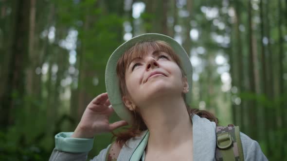 Happy Brunette Woman with Hat in the Forest Looks Around