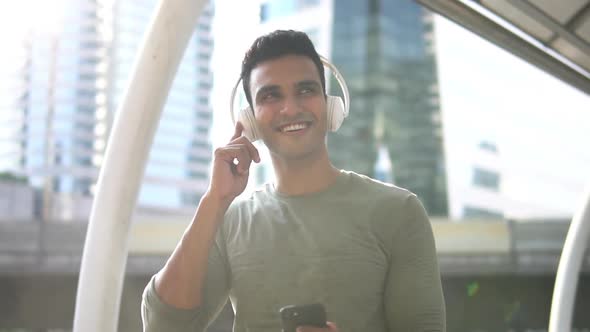 Portrait of a smiling young Indian man holding mobile phone in hand enjoying listening to music