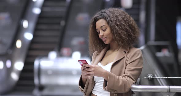 Female commuter using smartphone in front of escalator in London alt