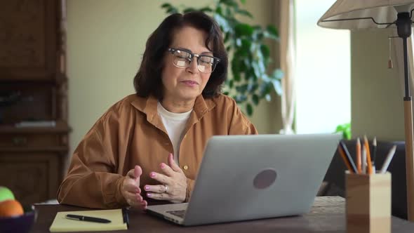 Woman Having Online Talk and Sitting at Table with Laptop in Home Room alt