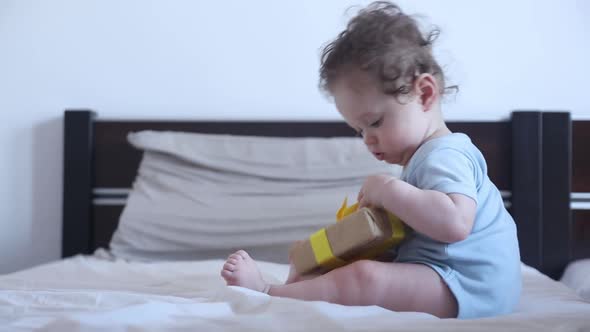 Little toddler boy play with gift box in bed