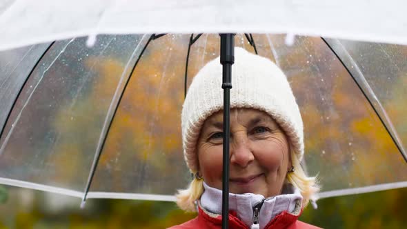 A Woman in a Red Jacket and Under a Transparent Umbrella Enjoying the Rainy Weather