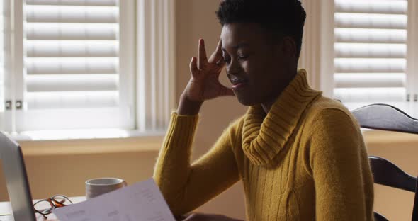 Stressed african american woman holding a document while working from home alt