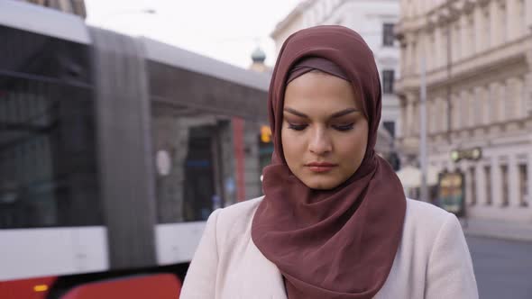 A Young Beautiful Muslim Woman Works on a Smartphone That's Off Camera in a Street in an Urban Area alt