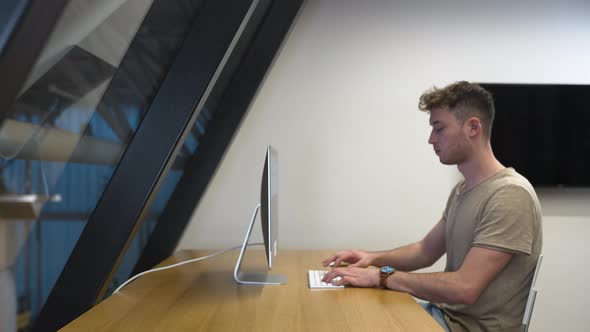 Young man in profile,casual dresscode,working on PC in a modern office. alt